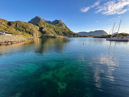 Quiet bay with clear blue waters and a sailboat, surrounded by green mountains and clear skies,