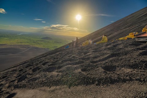 Group of adventurers sandboarding down a volcano at sunset. Tourists sandboarding on Cerro Negro,
