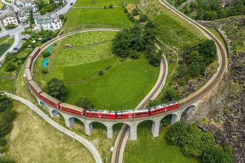 Red train of the Rhaetian railroad line, Bernina Express, passing the circular Brusio viaduct,
