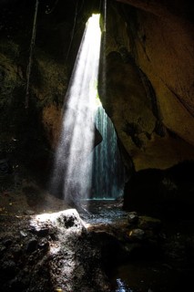 Light beam falls into a dark cave with a waterfall, creates a mysterious atmosphere, Tukad Cepung