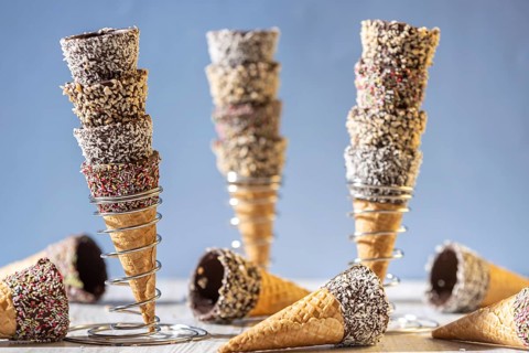 Ice cream cones stacked in metal stands, decorated with sprinkles and nuts