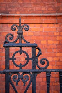 Detail, black ornate wrought iron fence in front of a brown-red brick wall, Chelsea, London,