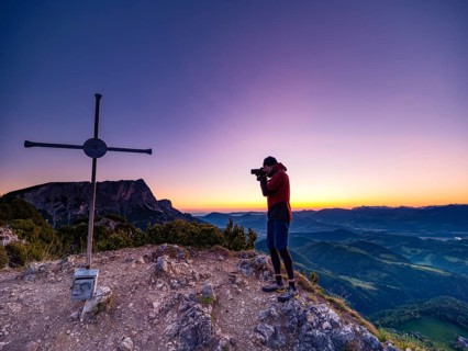 Photographer at dawn at Rauhen Kopf summit cross, Untersberg in the back, Berchtesgaden Alps,