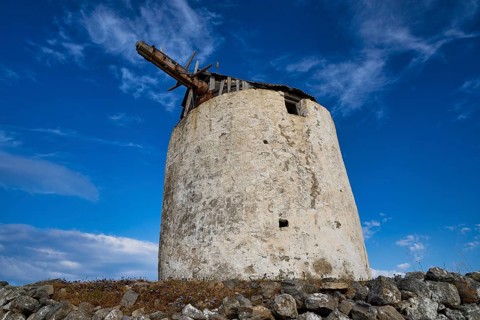 Old windmill tower against a deep blue sky with clouds, main town on Kimolos, Kimolos, Chorio,