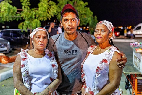 Three people in traditional clothes standing close together at night, visitors to a festival in