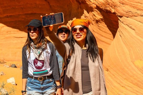Three young women smiling, taking a selfie with a smartphone, exploring biidi the arch cave in