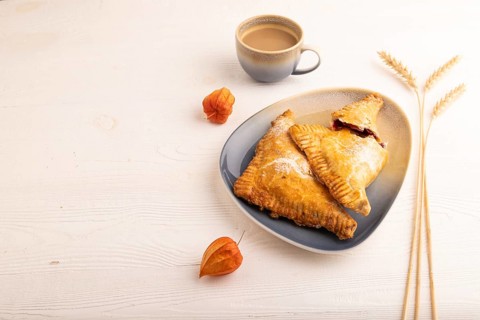 Triangles Pie, Puff Pastry, Samsa with cherry jam on white wooden background, cup of coffee, side
