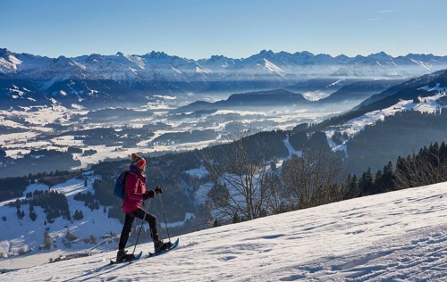 Nice and active senior woman snowshoeing in in the snow covered Allgaue alps above the valley of