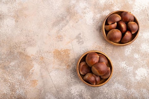 Wooden bowl with raw edible ?hestnuts on brown concrete background, top view, flat lay, copy space,