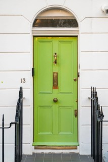 Light green front door with gold fittings in white house facade surrounded by black metal railing,