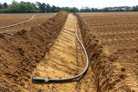 Poly pipe subsurface irrigation system in excavated ditch across sandy field, Shottosham, Suffolk,