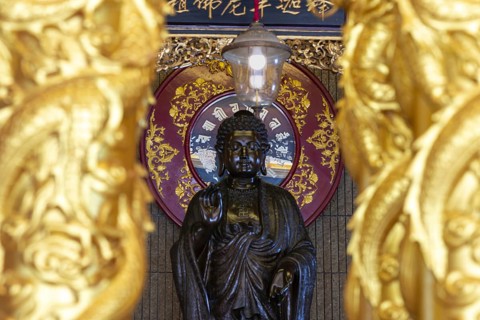 A standing Buddha in front of a richly decorated red mandala radiates quiet dignity and timeless