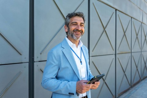 Smiling businessman wearing a blazer and id lanyard looking at camera while holding a digital