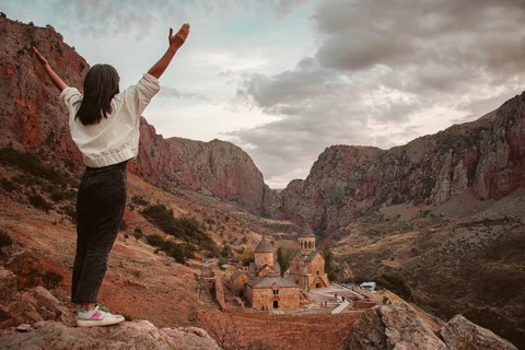 Excited happy tourist woman with outstretched arms admires the view of the famous Armenian