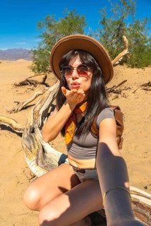 Young woman posing for a selfie, blowing a kiss into the camera lens while sitting on a weathered