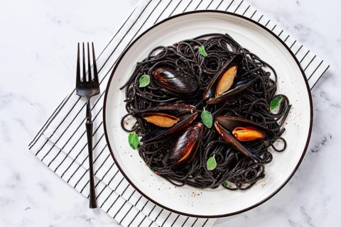Black spaghetti with mussels, on a white plate with a fork, on a striped napkin, marble background,