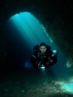 A diver with equipment explores an underwater cave illuminated by blue light rays, Fraskeric dive