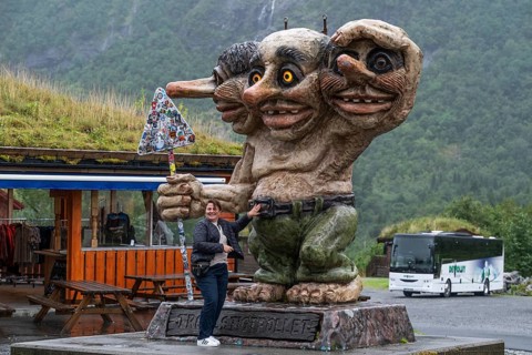 Sculpture of an oversized troll with three heads holding a sticker road sign, coach in the