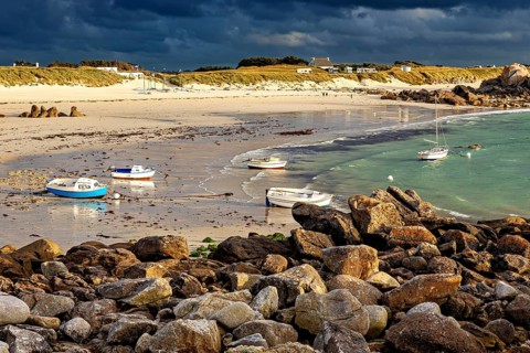 Beach with boats on water and rocks in the foreground under a cloudy sky, The coastal landscape