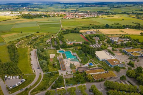 Large sports complex with swimming pools and surrounding fields under a cloudy sky, Herrenberg,