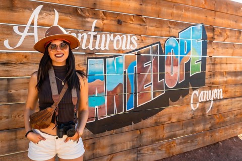 Young female traveler posing cheerfully in front of a handmade wooden sign depicting antelope