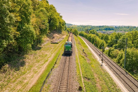 A train moves through a green landscape under a bright blue sky, electrification of the