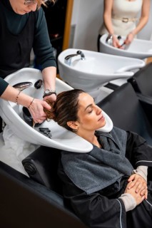 Hairdresser gently washing a relaxed woman's long dark hair at a modern salon sink, providing