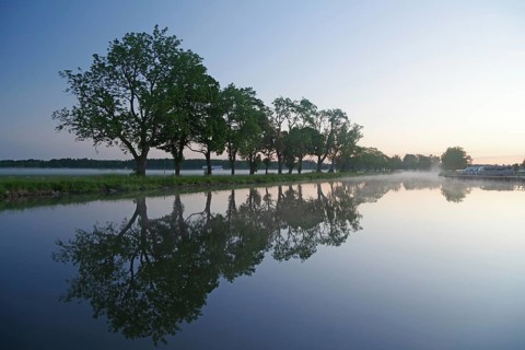 Trees reflect in calm water at dawn with light fog, Göta Canal, Töraboda, Västra Götalands län,