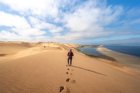 Woman in front of desert landscape, sand dunes and sea, Atlantic coast and sandy desert with sea of