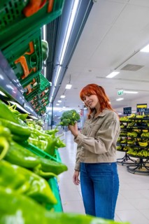 Redhead woman enjoying grocery shopping, selecting healthy green vegetables in the produce section