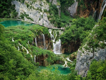 Tourists walk on a wooden walkway across majestic waterfalls and rivers surrounded by lush nature,
