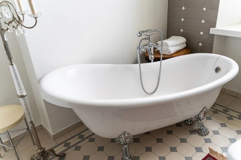 A white clawfoot bathtub with ornate metallic feet stands in a stylish bathroom. A wooden side
