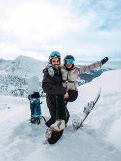 Young couple embracing and laughing on a snowy mountain summit with snowboards, enjoying an