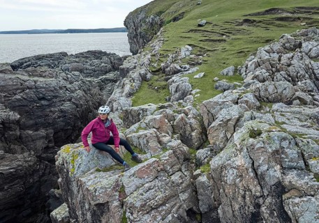 Nice senior woman resting during a bicycle tour in the rocky cliffs of Strathy Point in northern