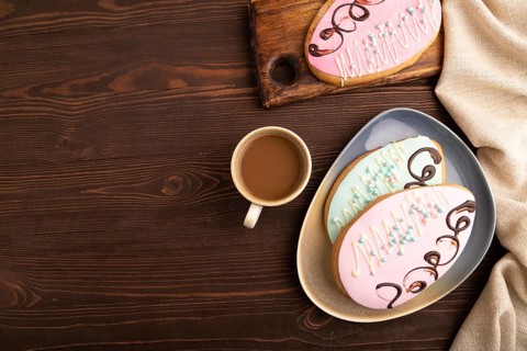 Glazed pink and blue decorated cookies, cup of coffee, on brown wooden background with linen