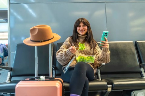 Woman travelers enjoying a healthy salad and using smartphone while waiting for a flight at the