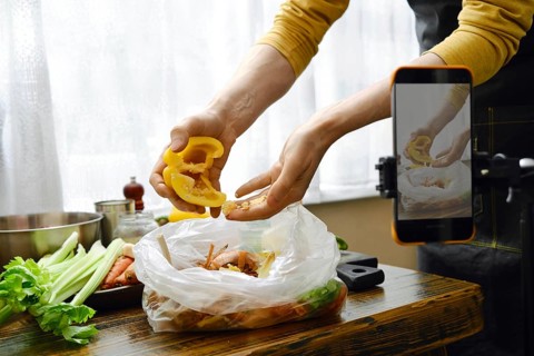 A person peels bell pepper from seeds and throws the waste into a compost bag. Food blogger records