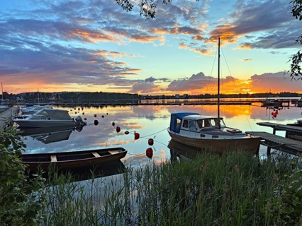Boats in quiet harbor at sunset with colorful sky and cloud reflections, Göta Canal, Karlsborg,