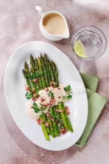 Fresh asparagus with cream sauce and bacon, on a white oval plate, light marble table, sunlight,