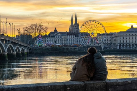 Young couple sits on a wall enjoying a colorful sunset over the adour river in bayonne, france,