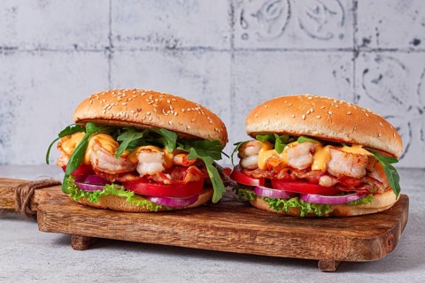 Two shrimp burgers and buns with sesame seeds, bacon, lettuce, tomatoes and onions, On a wooden