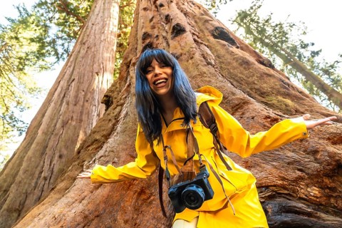 Happy young woman tourist wearing a bright yellow raincoat and carrying a camera, smiling and