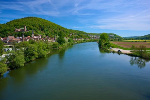 Picturesque river landscape with a village on the banks, surrounded by green hills and under a blue