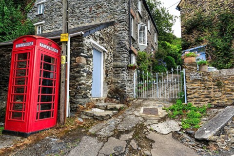 Red telephone box on a paved path next to a historic stone house, cottage, iron gate, Portloe,