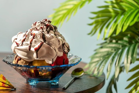 Sundae decorated with cream and chocolate next to green leaves