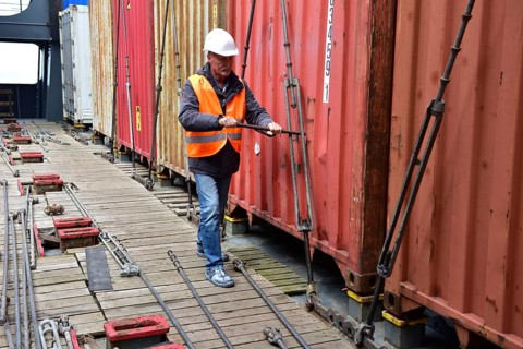 Worker with helmet secures containers on the bottom of the harbor with tension ropes, workers on