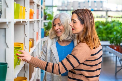 Mother and daughter smiling as they browse colorful ceramic plant pots on shelves in a garden