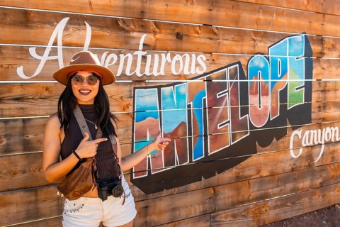 Smiling young woman traveler wearing a hat, sunglasses, and carrying a camera pointing at a