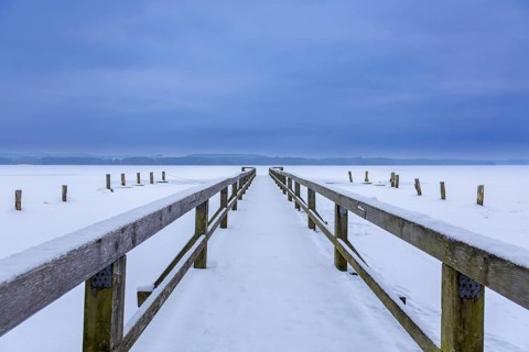 Wooden jetty at frozen Lake Ratzeburg, Ratzeburger See covered in snow in winter, Lauenburg Lakes