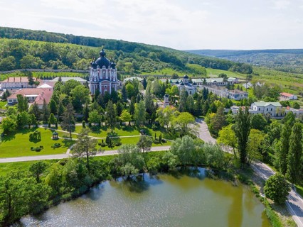 Landscape with a cathedral on the shore of a lake surrounded by well-kept gardens and hills, aerial